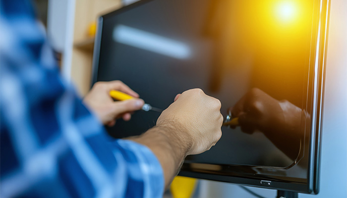 Un uomo con una camicia a quadri blu che usa un coltello con manico giallo per riparare uno schermo nero.
