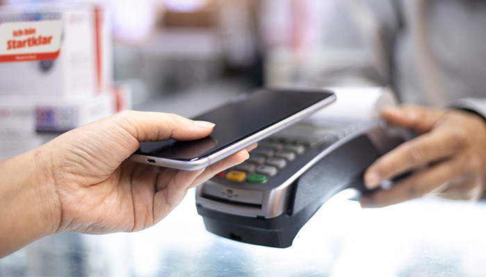 Una persona usa un telefono nero per pagare su un lettore di carte grigio e nero.