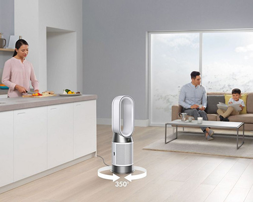 Interni di una casa: donna cucina, padre e figlio seduti sul divano, ventilatore Dyson in funzione.