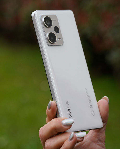 Una mano tiene un telefono bianco con due obiettivi della fotocamera su uno sfondo verde sfocato.