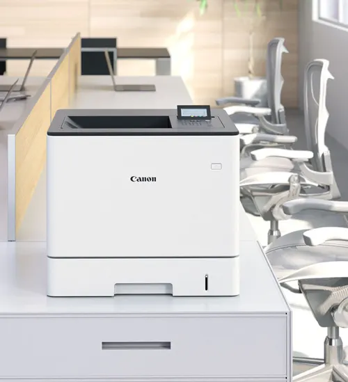 Stampante Canon bianca su mobile bianco in ufficio con scrivanie e sedie grigie sullo sfondo.