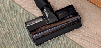 Aspirapolvere nero su tappeto verde e pavimento in legno chiaro.