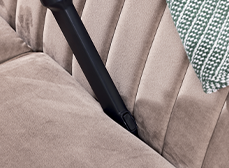 Aspirapolvere nero su divano beige con cuscino decorativo a motivi geometrici. Pulizia e manutenzione della casa.