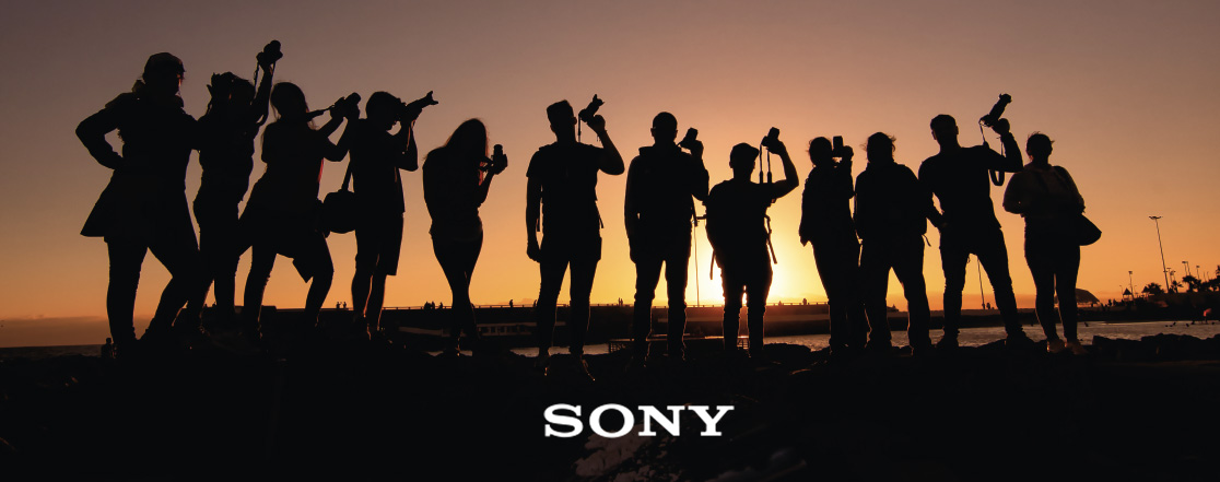 Silhouettes di persone con fotocamere al tramonto. In primo piano, il logo Sony.