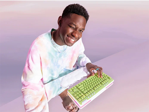 Un uomo sorridente con una felpa tie-dye tiene una tastiera verde e bianca su uno sfondo viola.