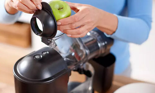 Donna inserisce mela verde in estrattore di succo nero. La macchina � su un tavolo di legno chiaro, sfondo luminoso.