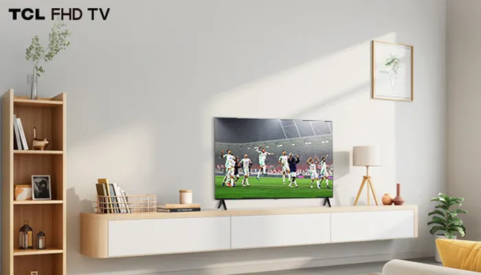 Soggiorno luminoso con TV che mostra una partita di calcio, mobile basso bianco, libreria in legno, lampada e piante.