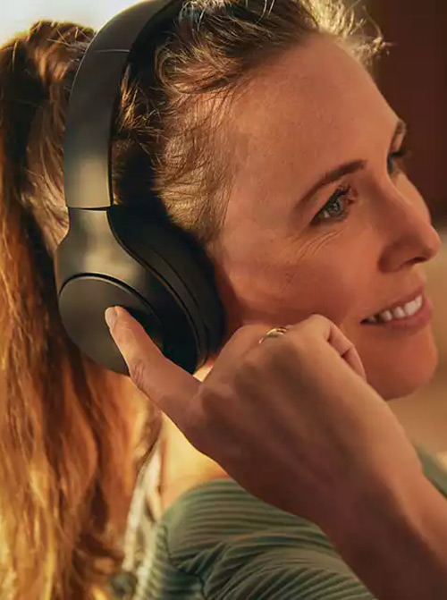 Donna con le cuffie che tocca l'auricolare destro; indossa una maglietta a righe verdi.