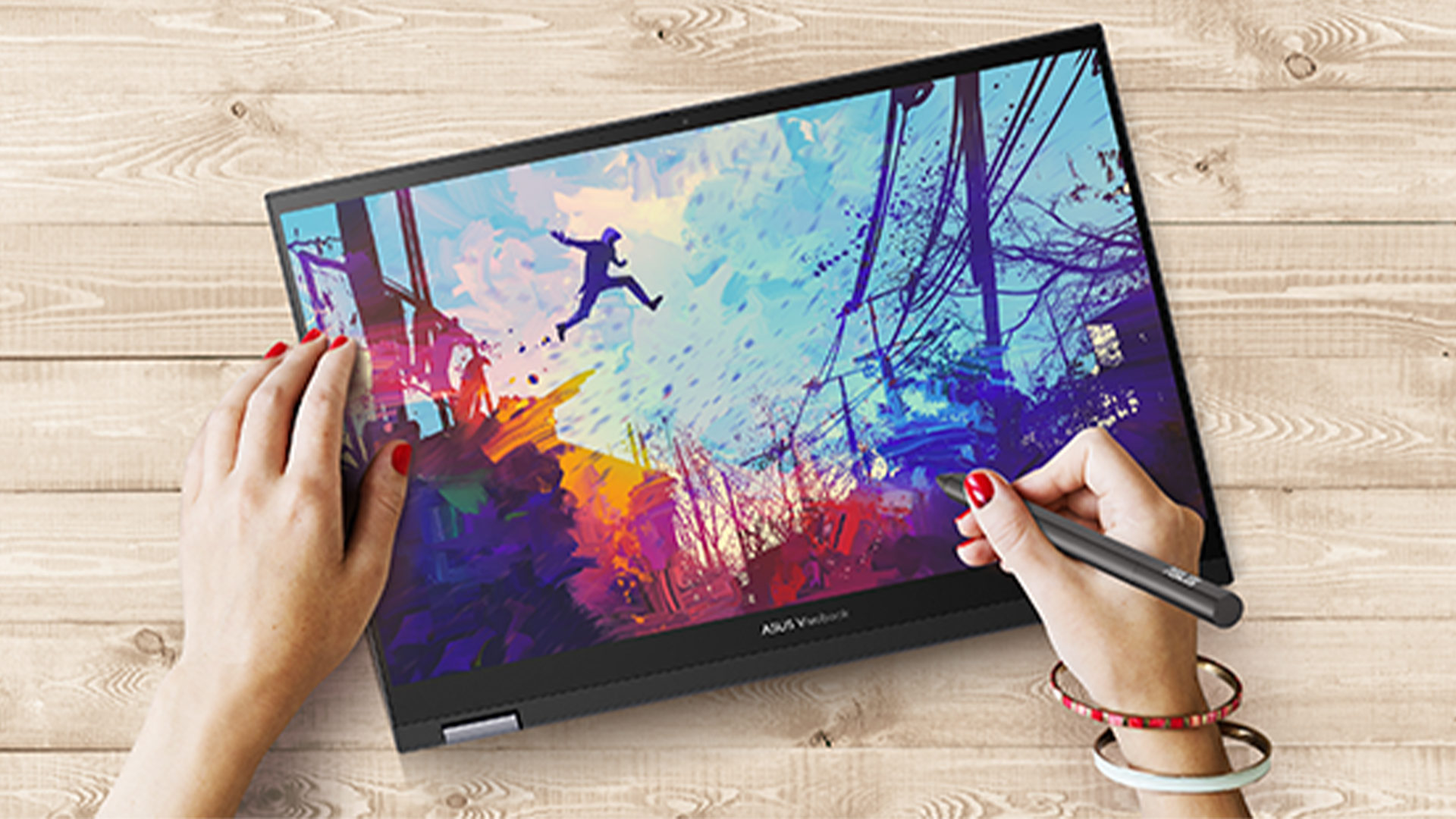 Un notebook aperto mostra un disegno colorato. Una persona usa una penna digitale sullo schermo su un tavolo di legno.