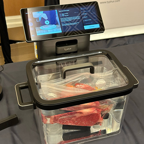 Macchina sous vide con schermo che mostra le istruzioni, contenitore trasparente con carne confezionata sottovuoto.