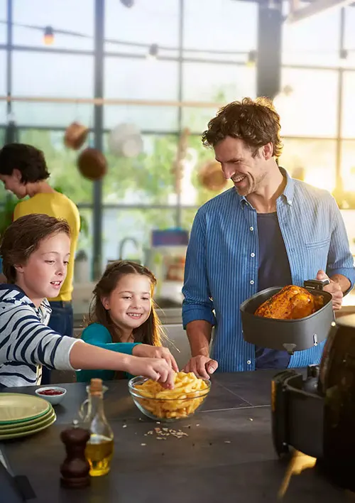 Interni luminosi con uomo che tiene una friggitrice ad aria accanto a bambini che prendono patatine fritte da una ciotola.
