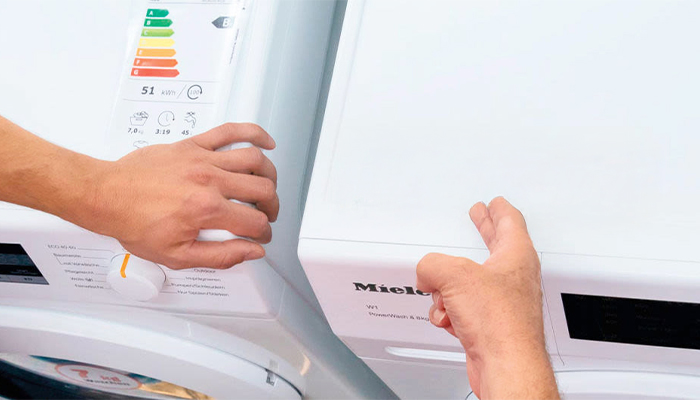 Lavatrice bianca Miele con etichetta verde "BETTER WAY". Una mano regola il selettore.