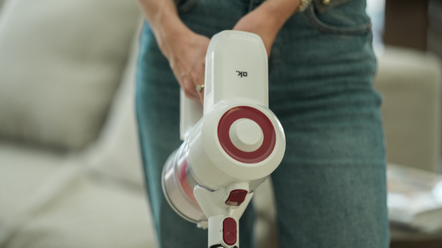 persona che tiene davanti a sé l'aspirapolvere a bastone bianco OHC 6125 con dettagli rossi nel soggiorno.