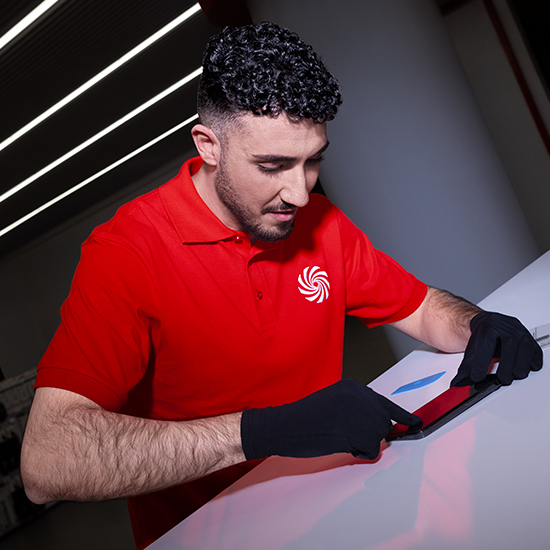 Un uomo in camicia rossa con guanti neri lavora su un tablet su una superficie bianca. Strisce luminose sullo sfondo.