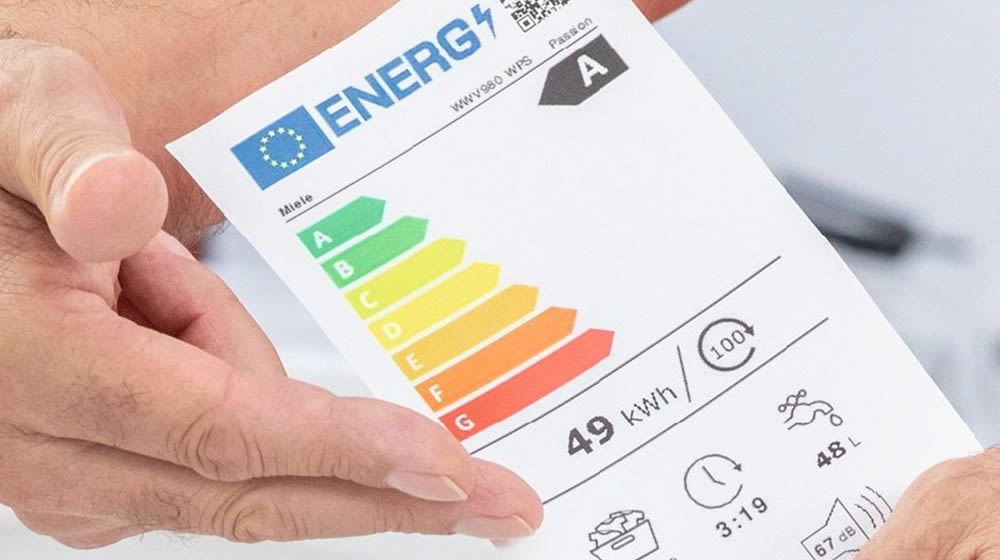 Etichetta energetica con classe A, consumi a 49 kWh, e indicazioni su acqua e durata ciclo, tenuta da mani.