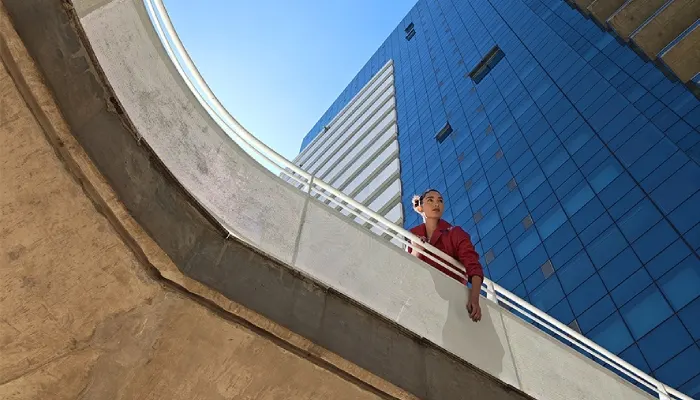 si vede un grattacelo dal basso e una donna che guarda in altro dal balcone