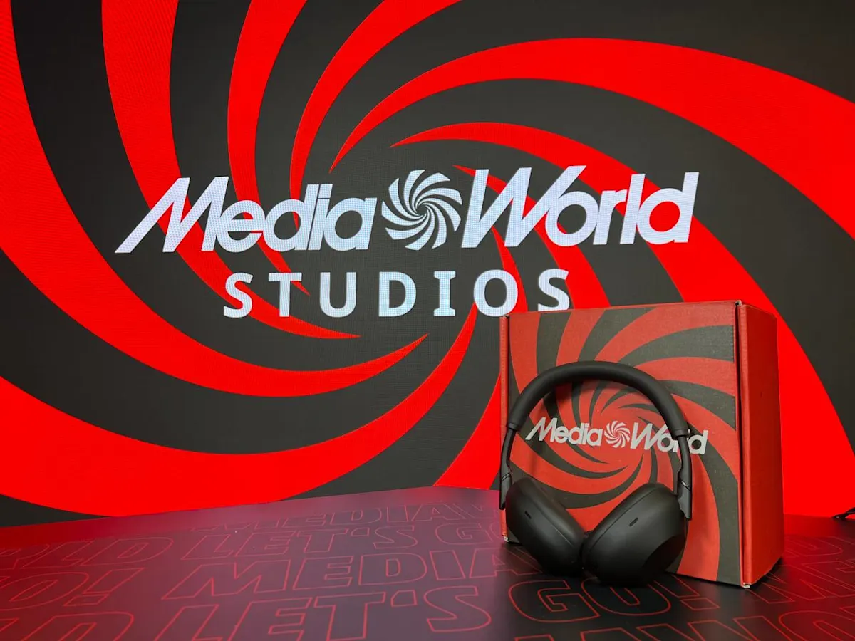 Cuffie nere davanti a scatola rossa con logo Media World. Sfondo rosso e nero con spirali e scritta "Studios" bianca.