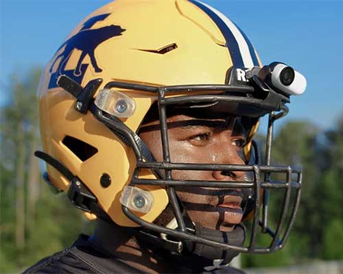 Primo piano di un giocatore di football americano con casco giallo, griglia nera e telecamera. Sul casco, un logo blu.