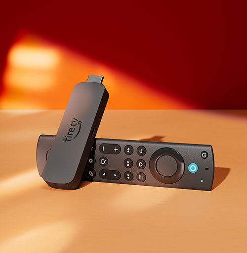Chiavetta Fire TV nera appoggiata a telecomando nero su sfondo arancione e rosso. Il telecomando ha pulsanti circolari.