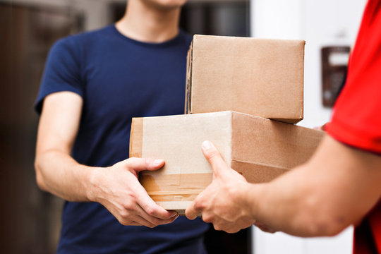 Due persone si scambiano scatole di cartone. Uno indossa una maglietta blu, l'altro una maglietta rossa.