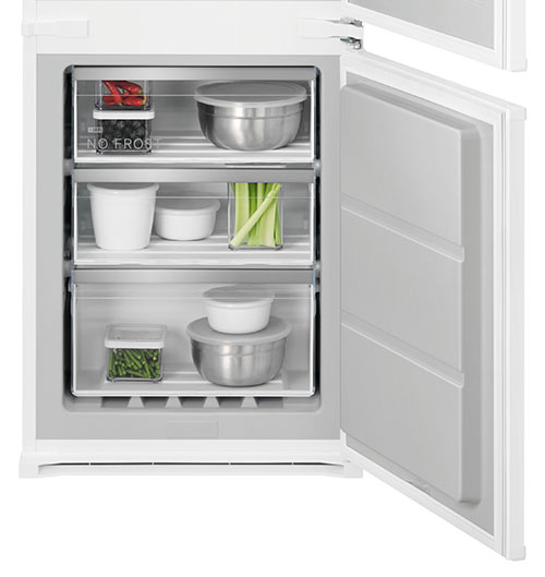 Frigorifero bianco aperto con contenitori di cibo su tre ripiani: verdure, frutta e ciotole in metallo.