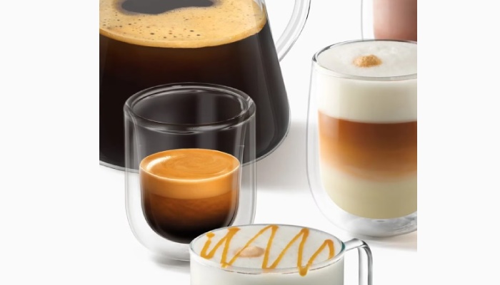 Tre bevande a base di caffè e latte in bicchieri di vetro, insieme a una tazza di caffè lungo con crema e a una bevanda decorata con schiuma e sciroppo.