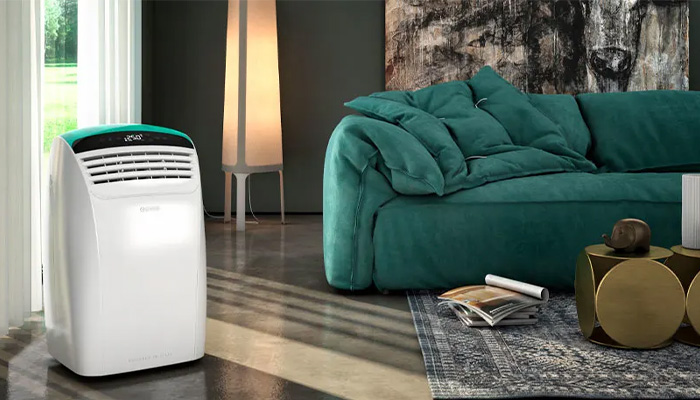 Soggiorno con condizionatore bianco, divano verde, lampada e tavolini dorati su tappeto decorato.