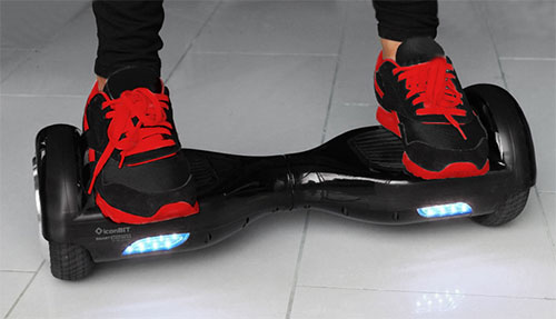 Scarpe nere e rosse su hoverboard nero con luci blu su pavimento bianco.
