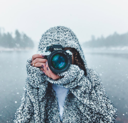 Una persona con una felpa con cappuccio tiene una fotocamera Nikon in un ambiente innevato all'aperto.