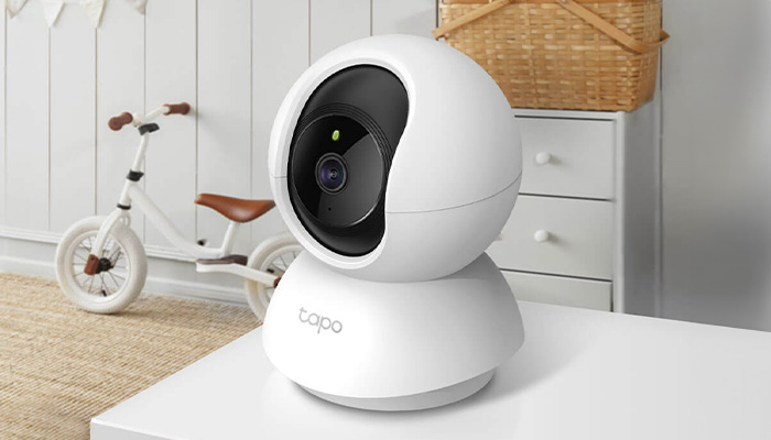 Telecamera bianca su tavolo bianco, con triciclo e cassettiera sullo sfondo.