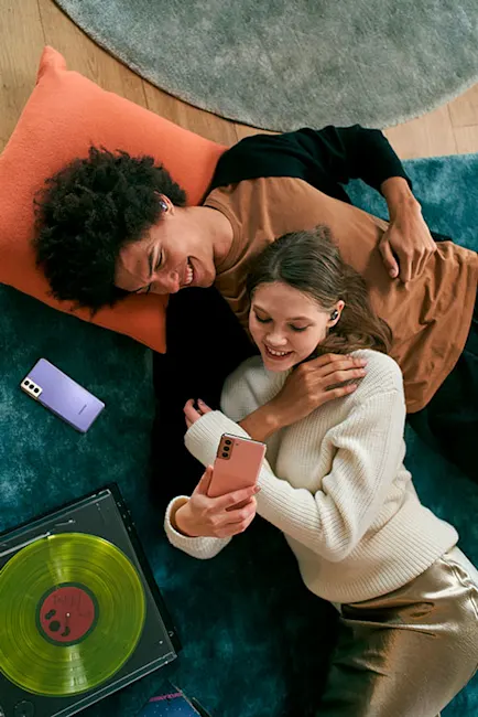 Una coppia sorride su un tappeto blu, con un telefono rosa. Accanto, un vinile verde e un altro telefono viola.