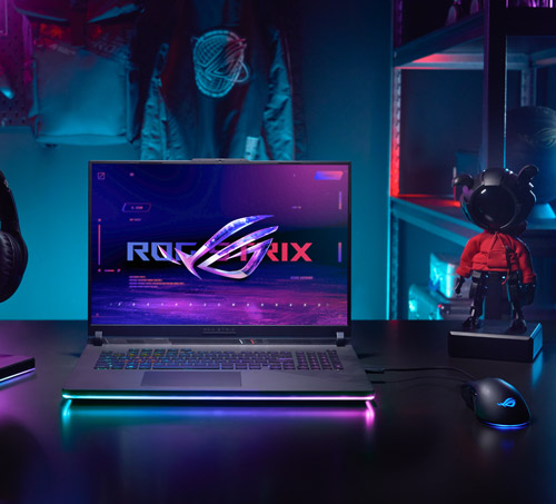 Un computer portatile mostra un logo su uno schermo viola. Un mouse e una statuetta sono sul tavolo. Uno scaffale � sullo sfondo.