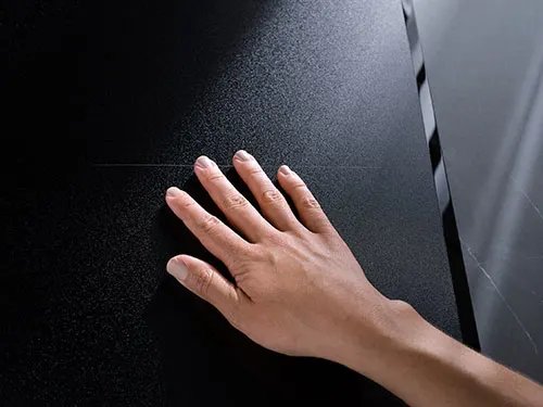 Una mano tocca una superficie nera liscia, con un riflesso chiaro sul bordo destro.