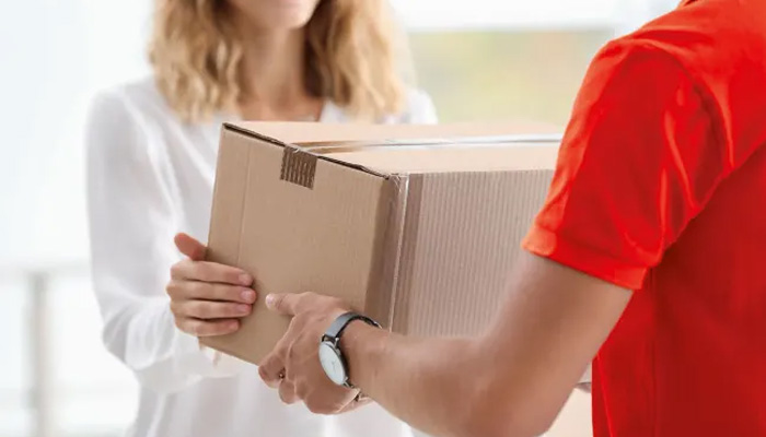 Un uomo in rosso consegna un pacco di cartone a una donna in bianco.