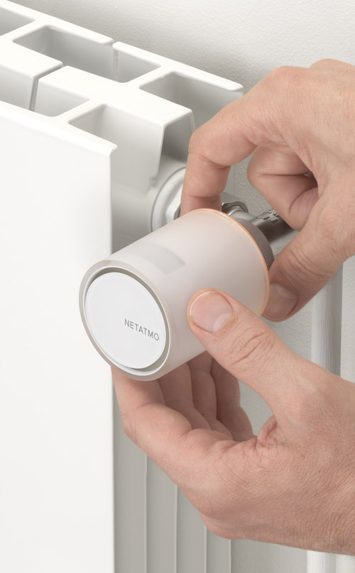Una mano regola una valvola termostatica bianca "Netatmo" su un termosifone bianco.