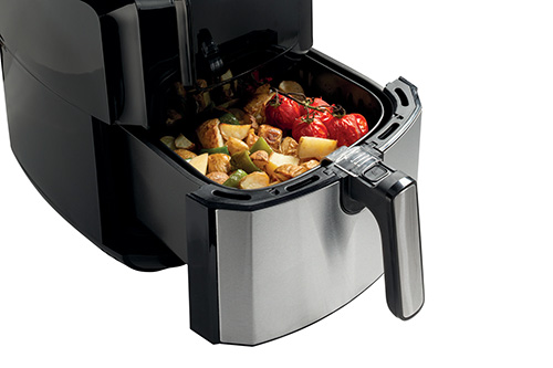 Friggitrice ad aria nera e argento con pomodori rossi e patate all'interno, su sfondo bianco.
