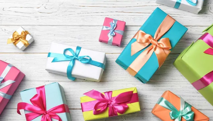 Scatola regalo colorata con fiocchi su tavolo di legno bianco. I colori includono rosa, verde, blu, giallo, bianco e arancione.