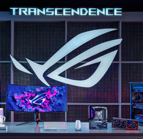 Scrivania con monitor, tastiera, mouse, microfono e componenti PC. Sullo sfondo, logo e scritta "Transcendence".