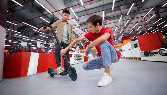 Due persone in un negozio esaminano un monopattino nero. Uno è in piedi sul monopattino, l'altro è accovacciato accanto.