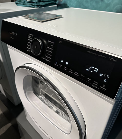 Lavatrice bianca con pannello nero e display digitale. Oblò circolare con bordo grigio.
