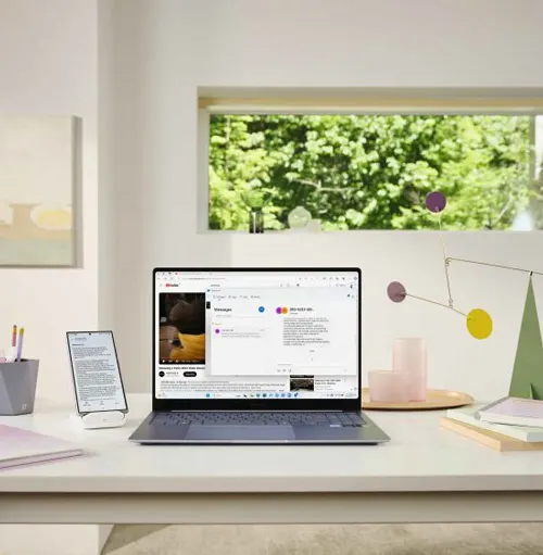 Scrivania bianca con laptop aperto, tablet, oggetti decorativi. Finestra con vista sul verde. Illuminazione chiara e naturale.