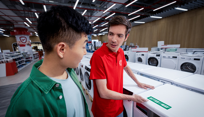 Un commesso mediaworld mosta una lavatrice con logo betterway ad un cliente in un negozio mediaworld