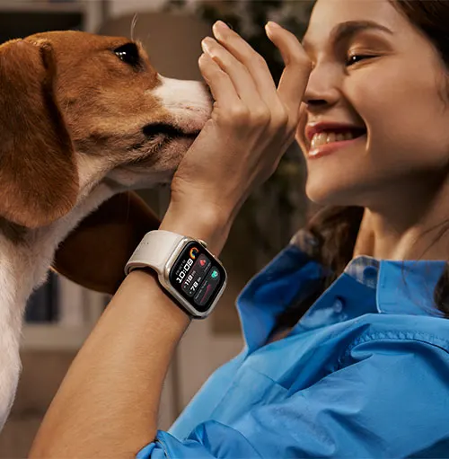 Donna sorridente con orologio al polso accarezza un cane marrone e bianco. Indossa una camicia blu.