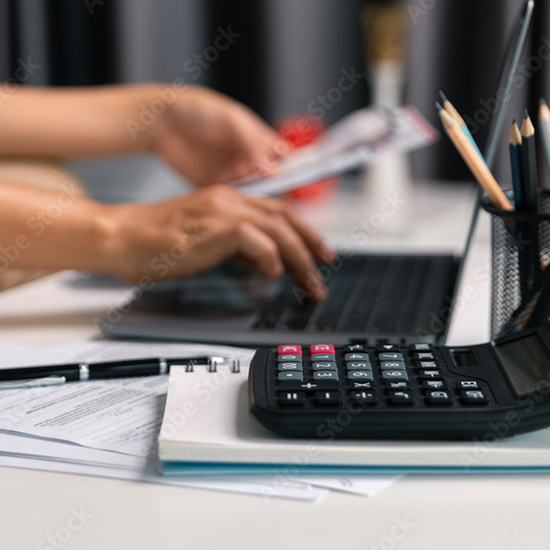 Mani su laptop, fogli, penna, calcolatrice nera su quaderno bianco. Portapenne con matite. Fondo sfocato, elementi d'ufficio.