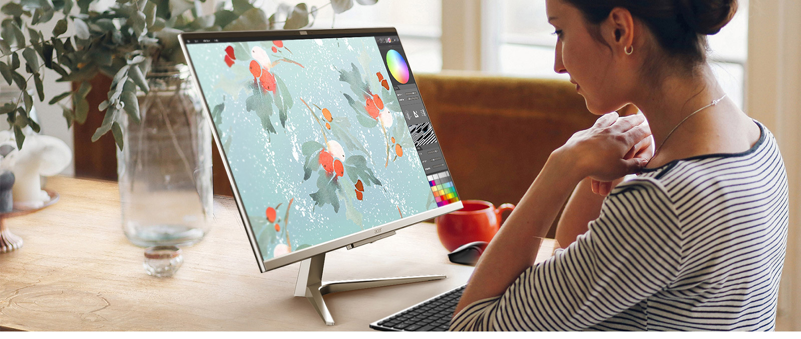 Una donna lavora a un computer con grafica floreale su una scrivania con una tazza rossa e una tastiera.