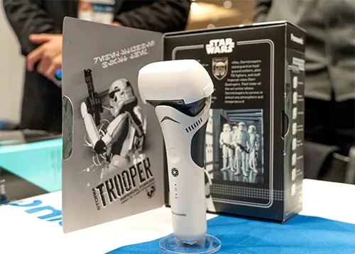 Rasoio elettrico bianco su base trasparente, confezione nera Star Wars, e cartellone con immagine di Stormtrooper.