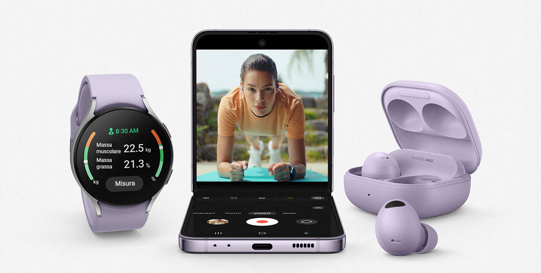 Orologio, telefono aperto con video di allenamento, cuffie e custodia lilla su sfondo bianco.