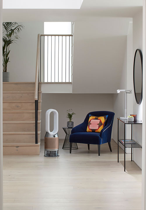 Interno luminoso con scale in legno, poltrona blu con cuscino colorato, purificatore d'aria e tavolino in metallo.