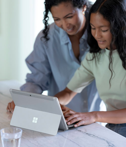 Madre e figlia usano un tablet grigio su un tavolo di marmo bianco. Un bicchiere d'acqua � sul tavolo.