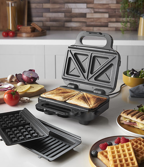 Cucina con tostapane aperto con toast dentro, piastre intercambiabili, verdure, waffle e panini.